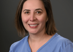 Headshot of Carmen Lenghel, a professional dentist, with a welcoming smile in a clinical setting.