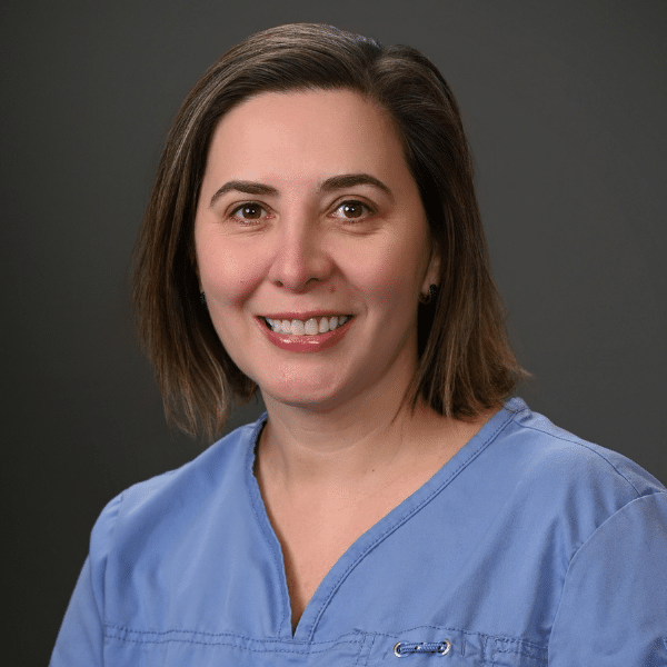 Headshot of Carmen Lenghel, a professional dentist, with a welcoming smile in a clinical setting.